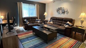 Ein modernes Wohnzimmer mit einer Sofagarnitur, einem Couchtisch, einem Fernseher und einem Schreibtisch mit einem Computer.