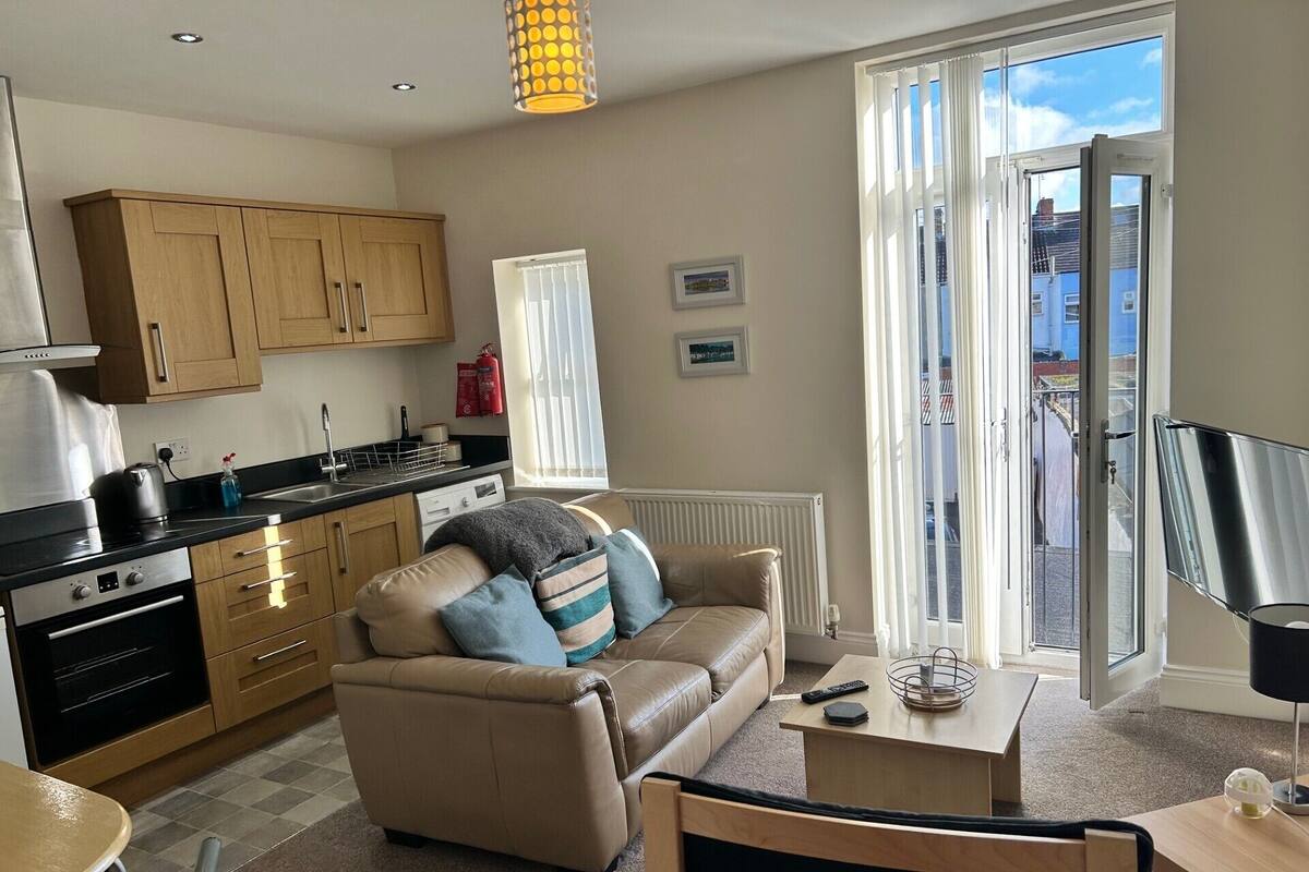A modern apartment with a kitchen, a living area with a sofa and armchairs, a dining table, and a balcony with a view.