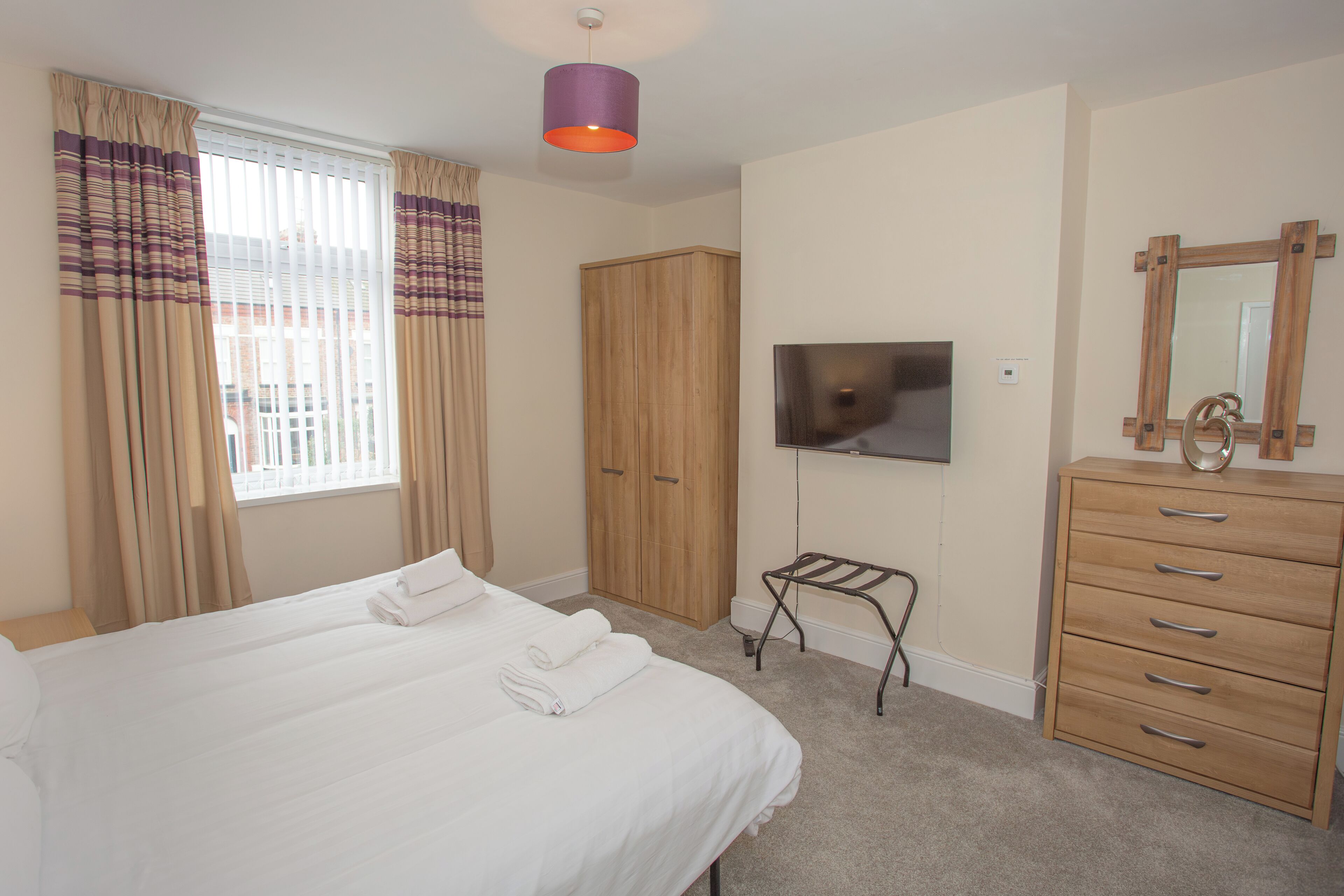 A hotel room with a large bed, a wardrobe, a television, and a mirror.