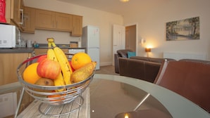 Une cuisine avec des meubles de rangement en bois, un réfrigérateur et un panier de fruits posé sur une table en verre.