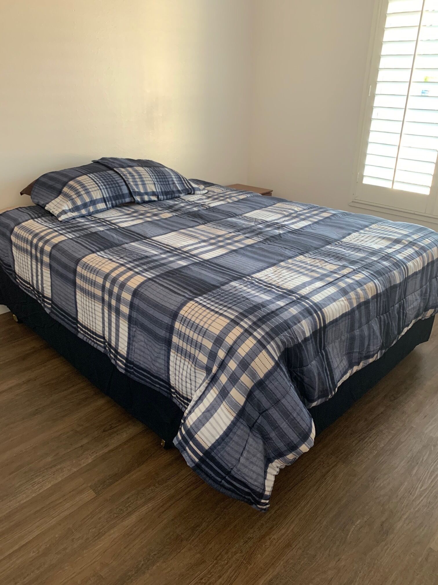 A bedroom with a bed, wooden flooring, and a window with blinds.