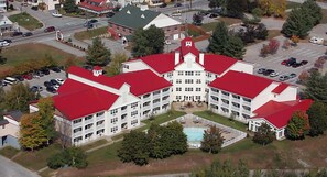 A large, multi-story building with a symmetrical facade, a central courtyard with a swimming pool, and a parking lot surrounding the property. - Franconia Notch State Park - South Mountain Resort (Lincoln)