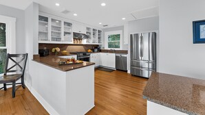 A modern kitchen with white cabinetry, stainless steel appliances, and a wooden floor. - Gorgeous views!  Charming home on the river (Kiawah Island)