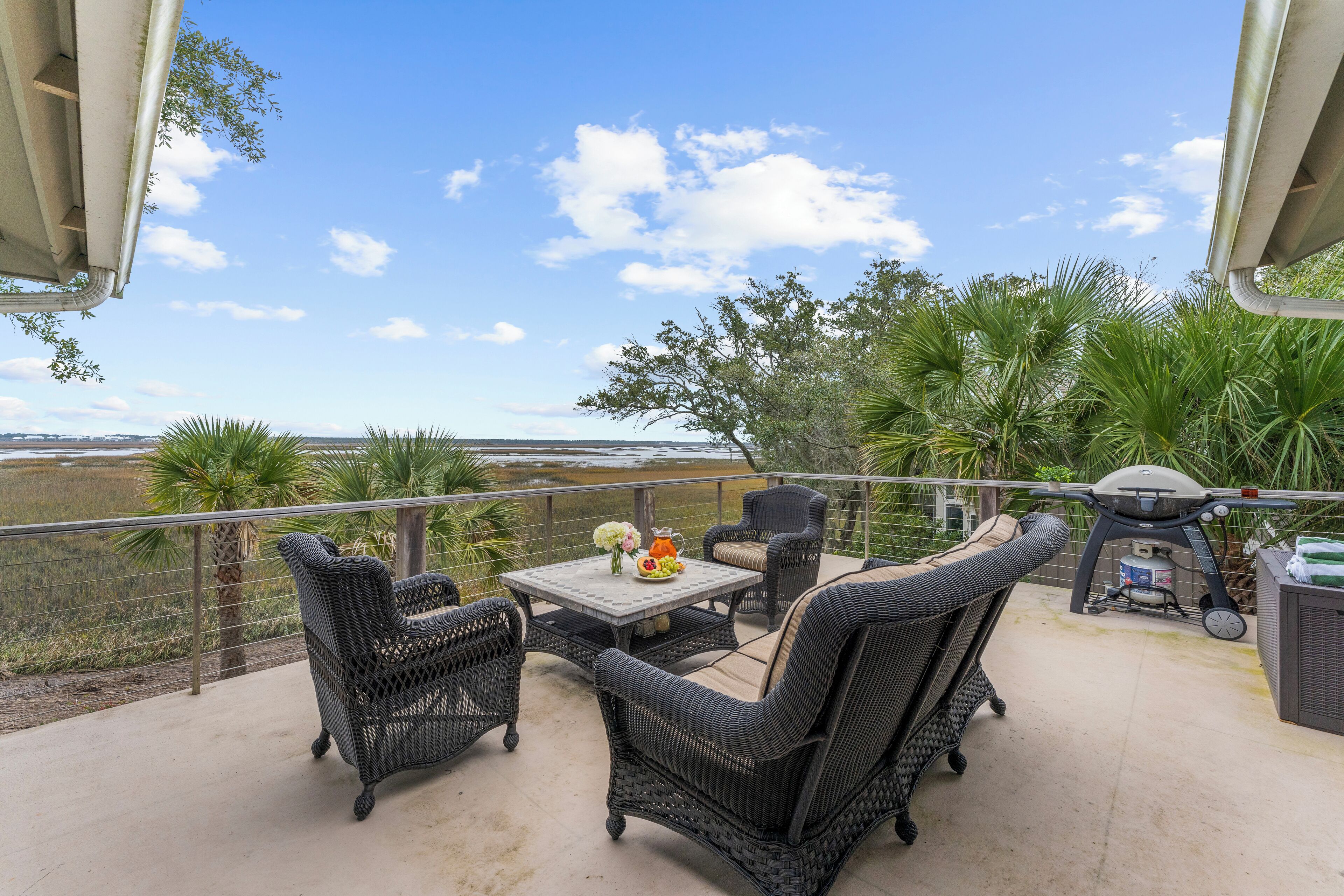A balcony with wicker furniture, a table with flowers, and a grill.