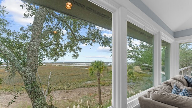 A room with a large window offering a view of a natural landscape, including a tree and grassy area. - Gorgeous views!  Charming home on the river (Kiawah Island)
