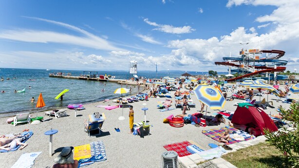A beach with umbrellas, lounge chairs, and a water slide.
