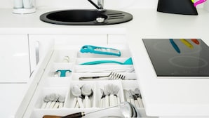 A kitchen with a black sink, white cabinets, and a drawer organizer with utensils.