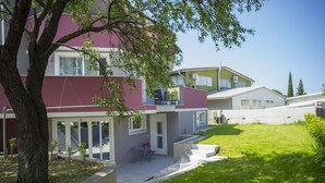 A modern residential building with a well-maintained lawn and a tree in the foreground.