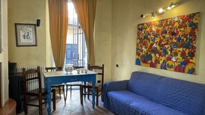 Una habitación con una mesa de comedor, sillas, un sofá azul, un radiador y un cuadro colorido en la pared.