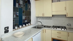 Cocina con estufa a gas, pileta y ventana con azulejos de colores.