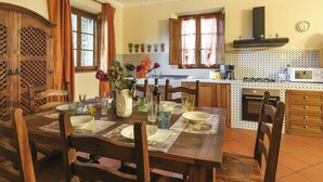 A dining area with a wooden table set for four, surrounded by chairs. There is a vase with flowers on the table, and a kitchen area is visible in the background with a microwave and stove. - Stunning private villa for 6 people with WIFI, A/C, private pool, TV, terrace and pets allowed (Capannori)