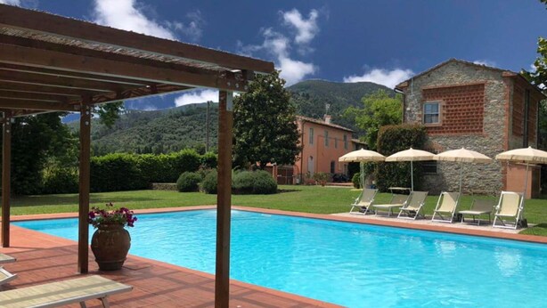 A swimming pool with lounge chairs and umbrellas, a pergola, and a stone building in the background. - Stunning private villa for 6 people with WIFI, A/C, private pool, TV, terrace and pets allowed (Capannori)
