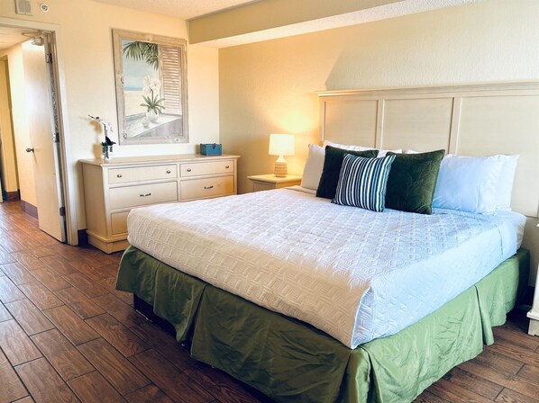 A neatly arranged bedroom with a large bed, a dresser, a nightstand, and a window with a view. - Stunning Oceanfront Suite w Jetted tub! (Myrtle Beach)