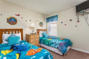 A bedroom with two beds, a nightstand, a lamp, a window with blinds, and wall decorations. - Vacation in Paradise (Kissimmee)
