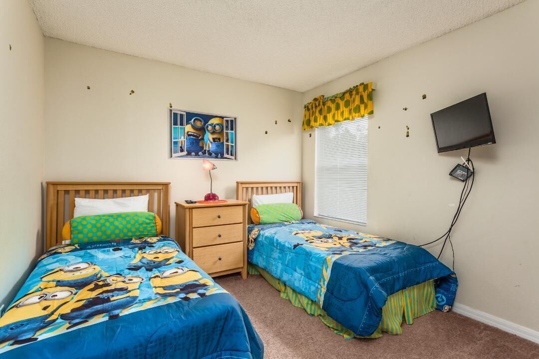 A bedroom with two beds, a nightstand, a TV, and a window with blinds.