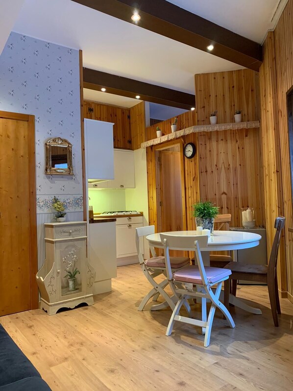 A cozy room with a wooden floor, a round table with chairs, a small white cabinet, and a clock on the wall.
