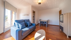 A modern living room with a sofa, a dining table, and a TV. - HomeHolidaysRentals Elodie - Costa Barcelona (Calella)
