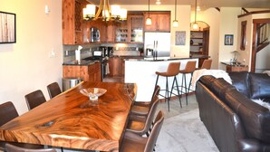 A modern kitchen with wooden cabinets, a central island, and a dining area with a large wooden table and leather chairs. - Gorgeous luxury top floor condo! Stunning Mountain Views! Private decks! Garage  (Fraser)