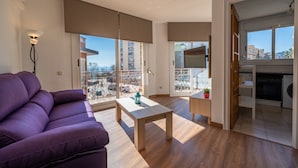 A modern living room with a purple sofa, a wooden coffee table, and large windows offering a view of the cityscape.