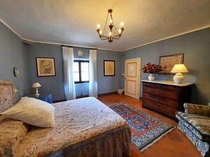 A bedroom with a bed, dresser, and chair, featuring a chandelier, curtains, and a rug. -  Pasqui Villas Historic Villa La Consuma San Giovanni D'Asso-Italy (SAN GIOVANNI D'ASSO)