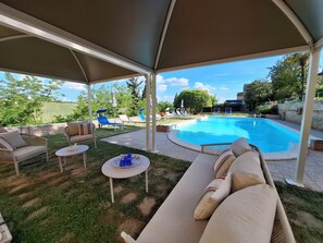 Un espace piscine extérieur doté de chaises longues, d’un coin salon abrité et offrant une vue sur le paysage environnant.