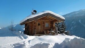 A wooden cabin with a snow-covered roof, surrounded by snow and mountains. - Nice apartment for 6 guests with WIFI, TV and balcony (Bramberg Am Wildkogel)