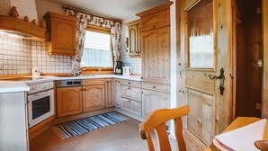 A kitchen with wooden cabinets, a stove, a sink, and a window with floral curtains. - Nice apartment for 6 guests with WIFI, TV and balcony (Bramberg Am Wildkogel)