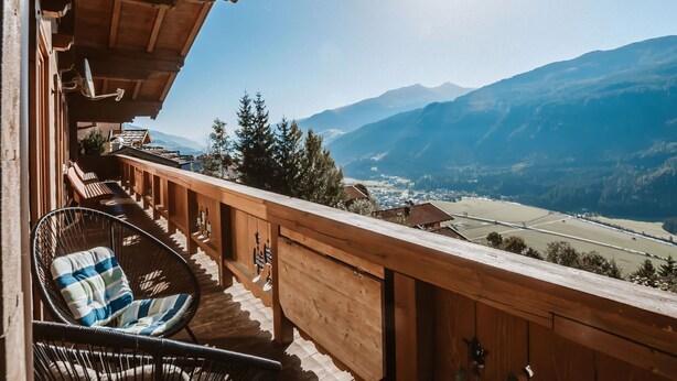 A wooden balcony with a wicker chair and a view of a valley and mountains. - Nice apartment for 6 guests with WIFI, TV and balcony (Bramberg Am Wildkogel)