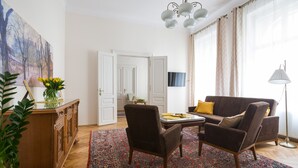 Un salón con un sofá, dos sillones, una mesa de centro, un aparador de madera, un cuadro, un televisor y una alfombra estampada.