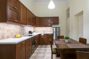 A kitchen with wooden cabinets, a stainless steel refrigerator, a dining table with chairs, and a potted plant on the table. - Belle Epoque II, luxury suite 50m to Main Square (Kraków)