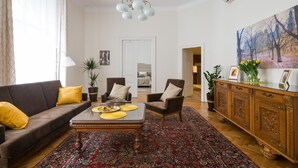 Una sala de estar con un sofá, sillones, una mesa de centro, un tapete estampado, un aparador y un cuadro en la pared.