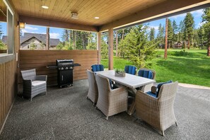 An outdoor patio with a grill, wicker furniture, and a view of a green landscape.