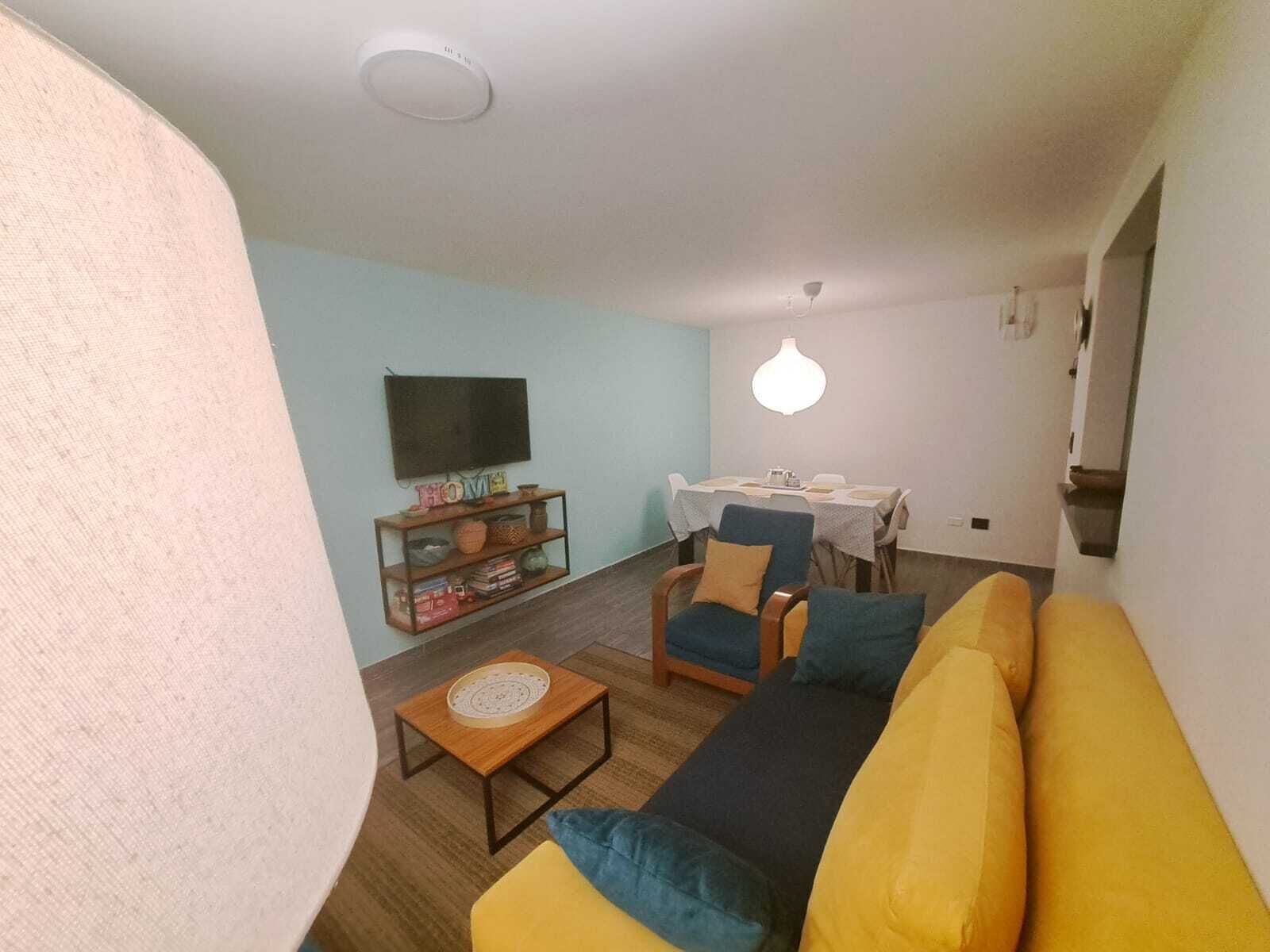Una sala de estar con un sofá, una mesa de centro, un televisor y un comedor con una mesa y sillas.