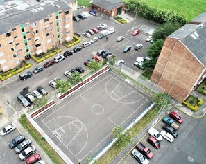 Vue aérienne d’un parking où sont garées plusieurs voitures, d’un terrain de basketball et des bâtiments environnants.