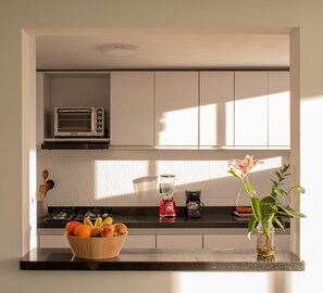 Une cuisine moderne avec des armoires blanches, un four à micro-ondes, un grille-pain, un mixeur et une machine à café posés sur le plan de travail.