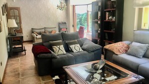 Un salón con un sofá gris, una mesa de centro de vidrio y una estantería.