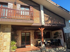 A two-story building with a balcony, stone walls, and a covered patio area with outdoor furniture.