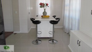 A dining area with a white table, two black chairs, a vase with flowers, and a fruit bowl. - Princess Vacation Home (Richwood)