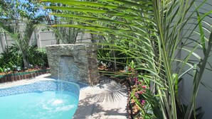 A swimming pool with a stone waterfall feature, surrounded by tropical plants and a stone wall. - Princess Vacation Home (Richwood)