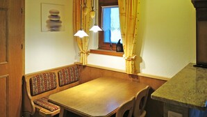 Une table à manger en bois, accompagnée d’un banc, de deux suspensions et d’une fenêtre avec des rideaux.