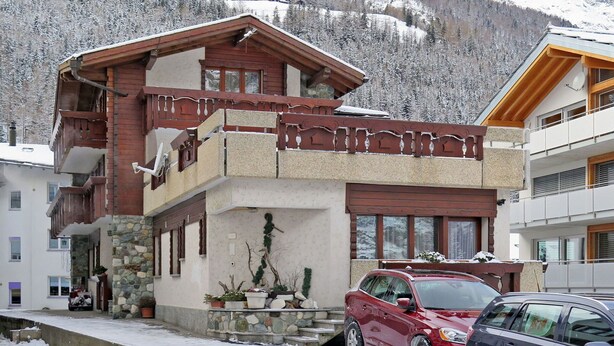 Un bâtiment à deux étages doté d’un balcon, de fondations en pierre et offrant une vue sur des montagnes enneigées.