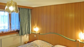 A bedroom with a wooden headboard, a floral bedspread, a hanging light fixture, and two bedside lamps.