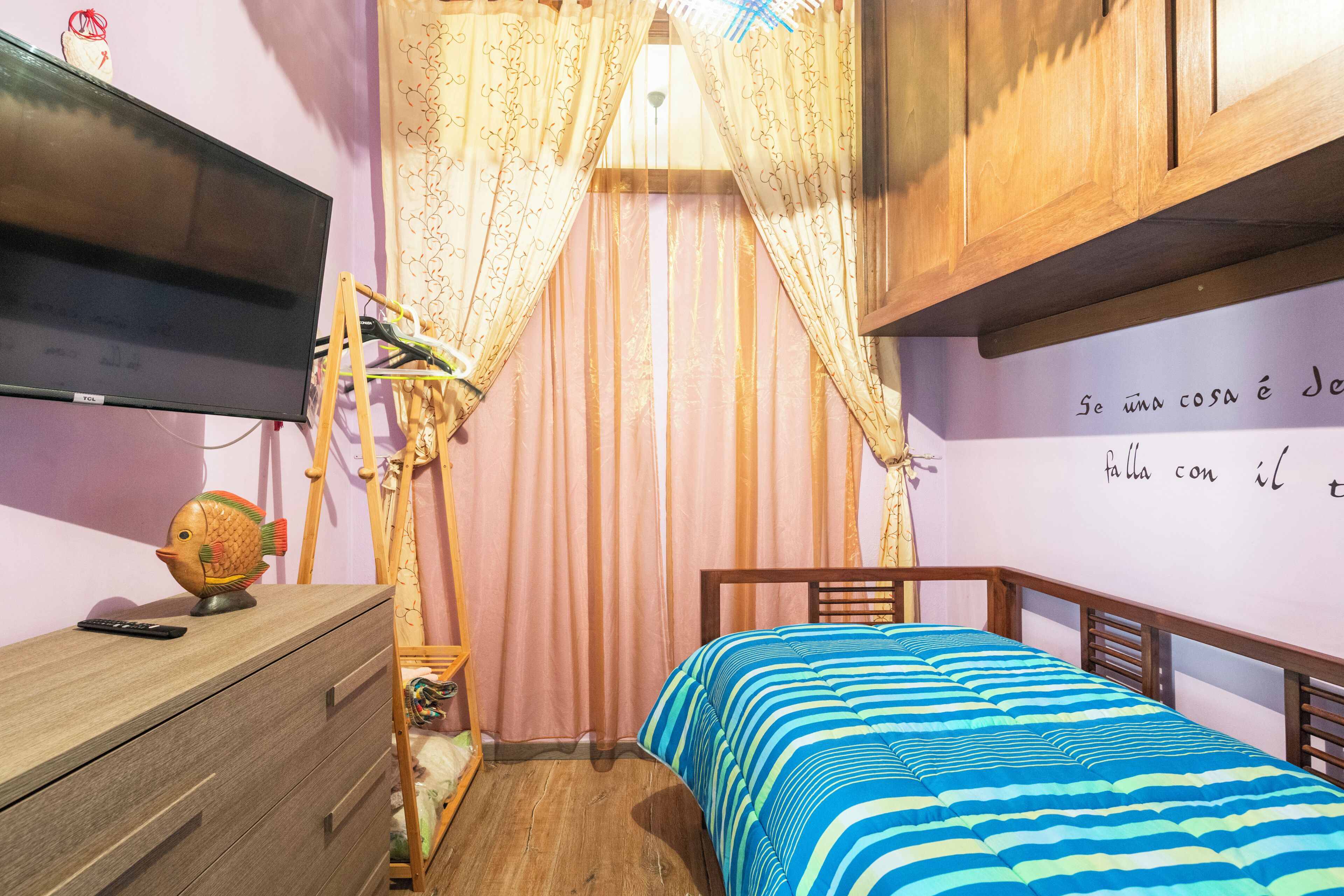 Ein Schlafzimmer mit einem Bett, einem Schminktisch, einem Fernseher und einem Vorhang.