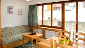 A cozy room with a sofa, a table with fruit, a radiator, and a window with a view of the outside.