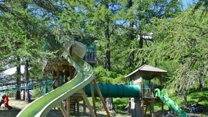 A playground with a green slide and a wooden climbing structure.