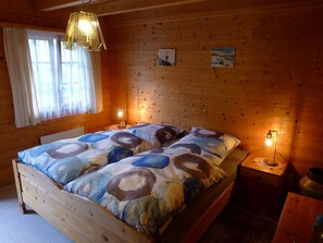 Accogliente camera in baita di legno con un letto, due lampade a parete e una finestra con tende.