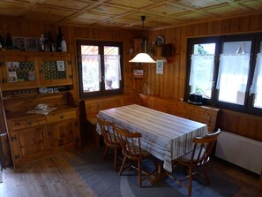Una baita di legno con un tavolo e sedie, armadietti in legno e una finestra con tende.