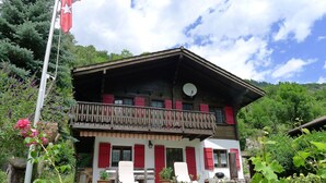 Een chalet met balkon, rode luiken en een tuin.