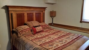 A bedroom with a wooden headboard, patterned bedding, and a bedside lamp. - Georgetown Lake, Discovery and the Pintlers (Anaconda)