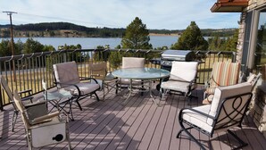 Een terras met buitenmeubilair, een barbecue en uitzicht op een meer en bos.